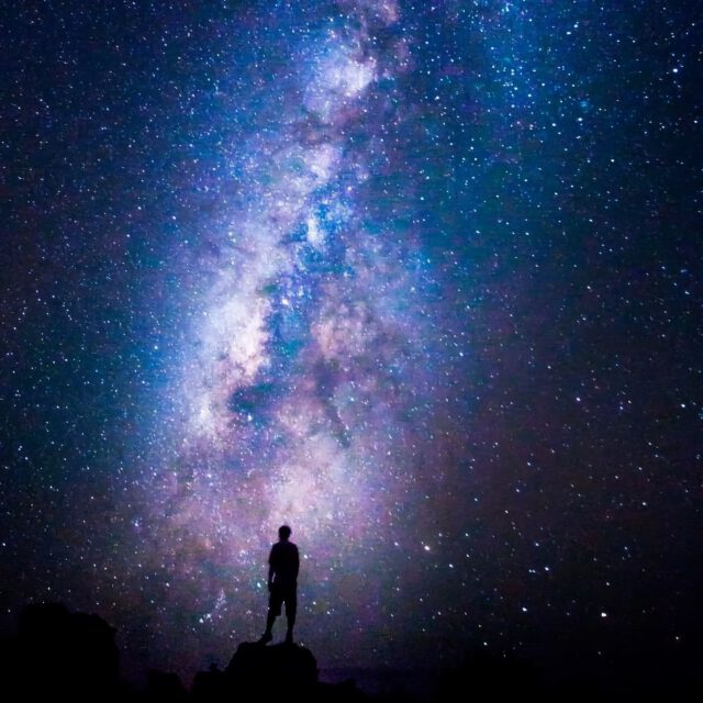 A man standing n tp of Mauna Kea gazing at the stars and milky wy galaxy
