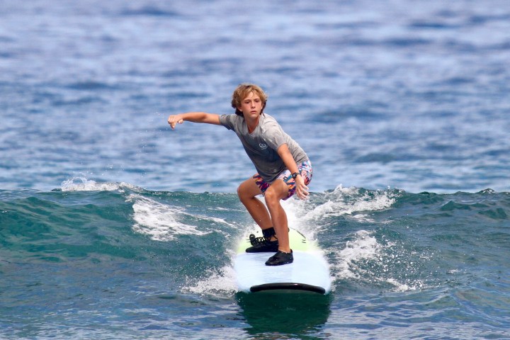 Young surfer balancing on a surfboard in the ocean.