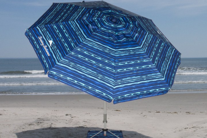 Blue beach umbrella on sandy shore with ocean backdrop.