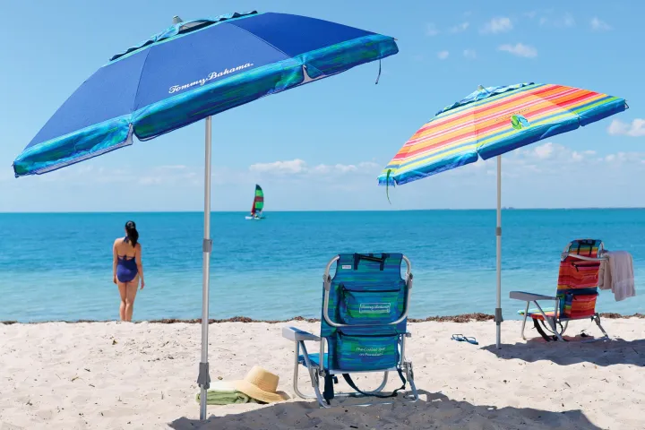 Beach scene with two umbrellas, chairs, a woman, and windsurfer.