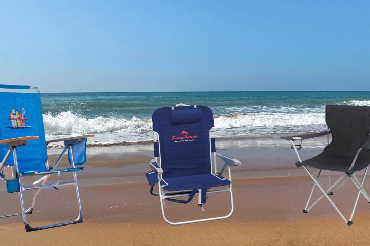Three beach chairs on sand facing the ocean waves and blue sky.