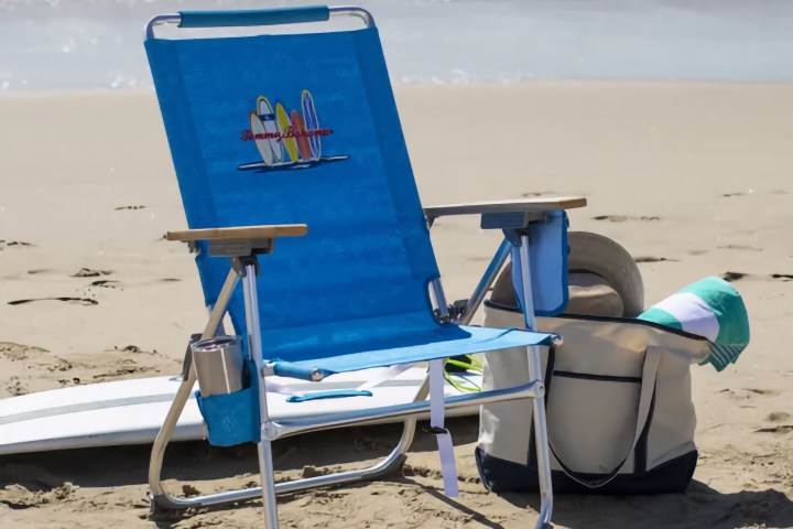 Blue beach chair with surfboard design on sand, ocean waves in background.