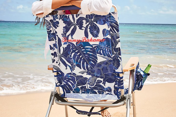 Person on beach chair with floral pattern, sandy beach, ocean waves, and clear sky.
